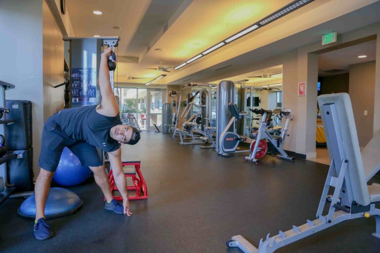 Man performing a side stretch with a kettlebell in a modern gym setting, emphasizing personal training and fitness routines in Austin.