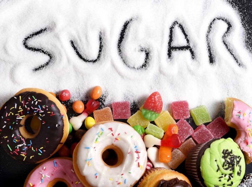 Assorted sugary snacks including donuts, cupcakes, and candy with the word 'SUGAR' written in granulated sugar