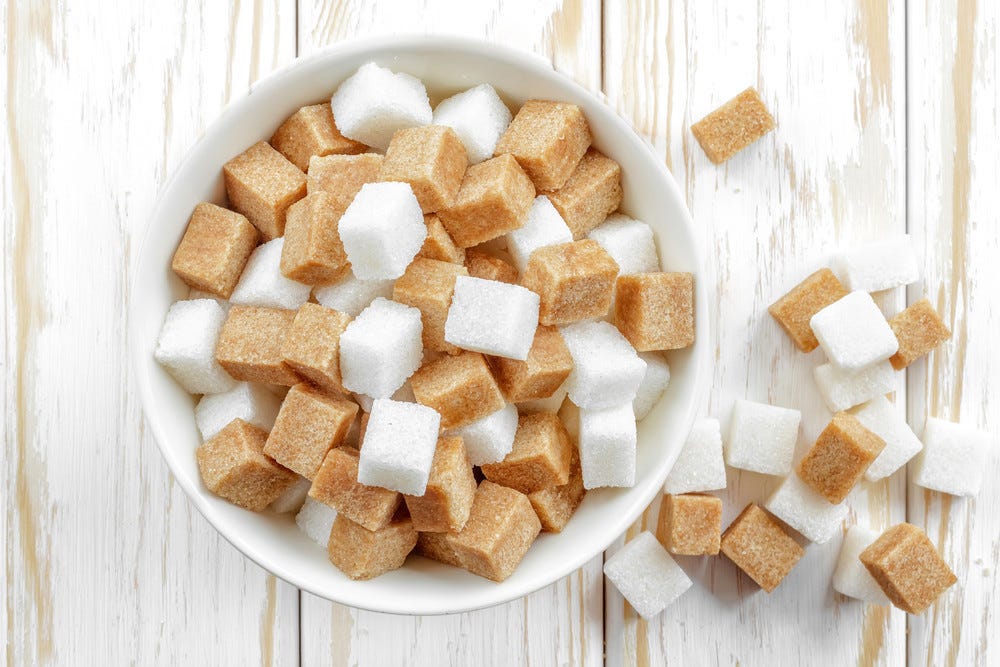 A bowl filled with white and brown sugar cubes on a white wooden surface