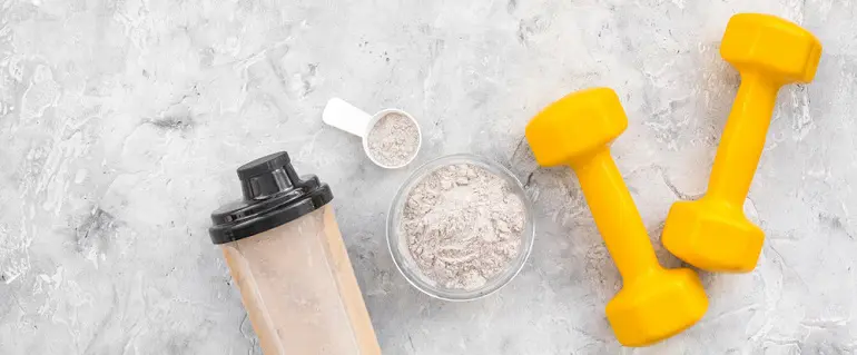 Whey Protein and Strength Training Essentials A protein shaker bottle, scoop of whey protein powder, bowl of powder, and yellow dumbbells on a light gray background.