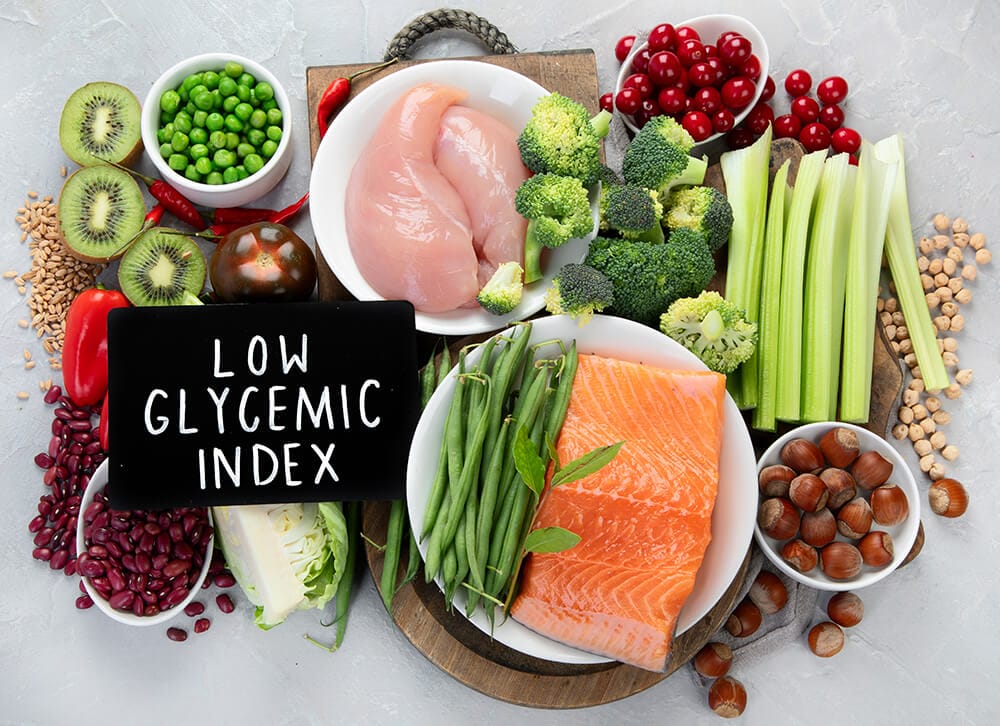 A selection of low glycemic index foods such as salmon, chicken breast, kiwi, broccoli, celery, beans, and berries on a wooden platter.