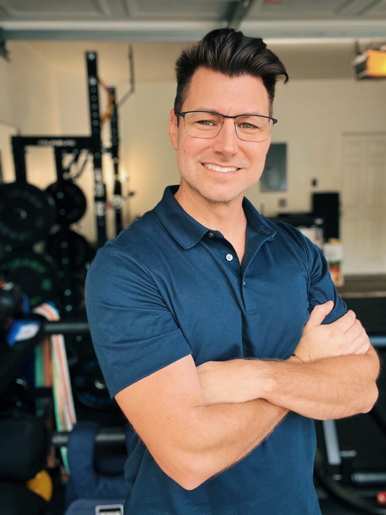 Justin, personal trainer at RxFit, smiling with arms crossed in a gym setting, emphasizing strength training and corrective exercise expertise.