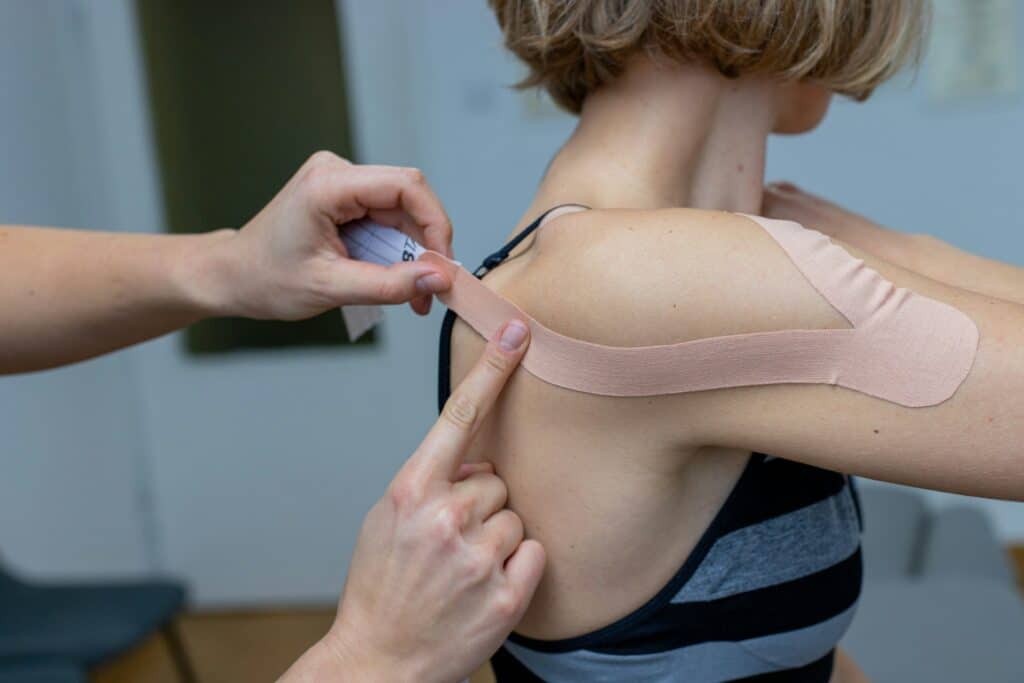 Person receiving shoulder taping treatment, demonstrating injury management and rehabilitation techniques for shoulder pain relief.