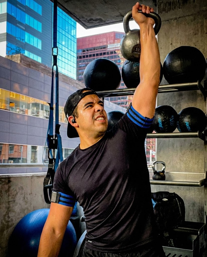 Man performing overhead kettlebell press in a modern gym setting, showcasing strength training and fitness, relevant to personal training and muscle preservation discussions.